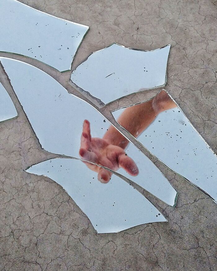 Broken mirror pieces on the ground, reflecting a hand, illustrating a common superstition.