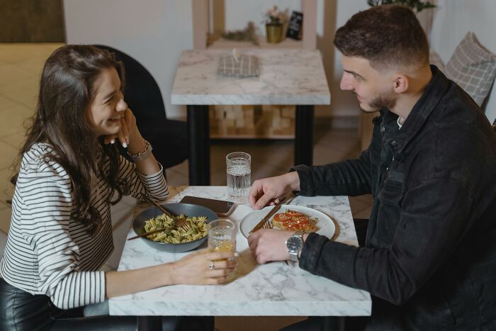 A couple enjoying a meal at a marble table, chatting and smiling, embodying brilliant life hacks for dining out.