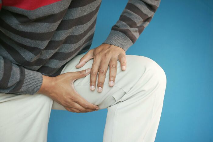 Person holding their knee, wearing striped shirt and beige pants, depicting genetic blessings and weaknesses theme.