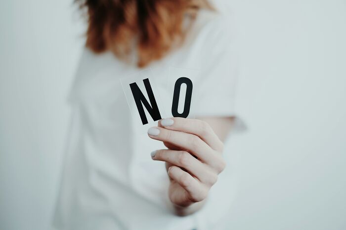 Person holding two pieces of paper forming the word "NO," illustrating work skills people lack in assertiveness.