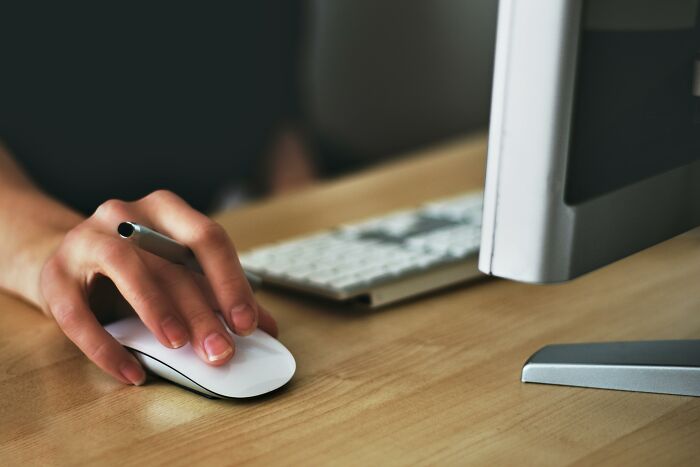 Hand using a mouse next to a keyboard and monitor, depicting work-struggles in an office setting.