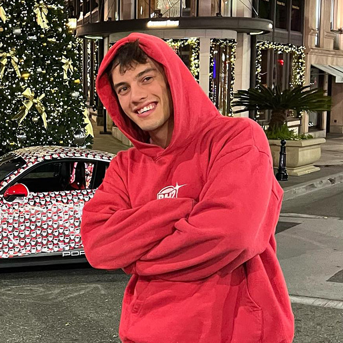 Man in red hoodie smiles with decorated car and Christmas tree in background. Man in red hoodie smiles with decorated car and Christmas tree in background.