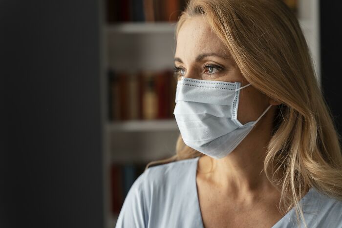 Woman wearing a mask, highlighting hygiene habits, with bookshelves in the background.