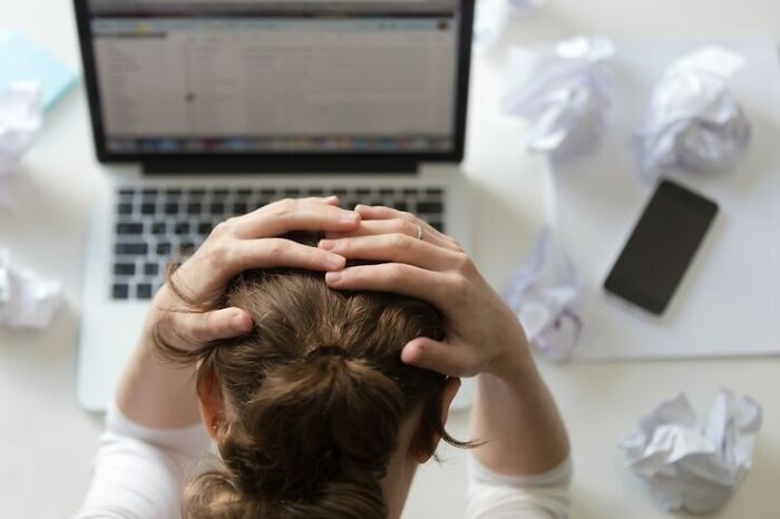 Person stressed at desk, hands on head, laptop and crumpled papers around, representing genetic blessings and weaknesses.