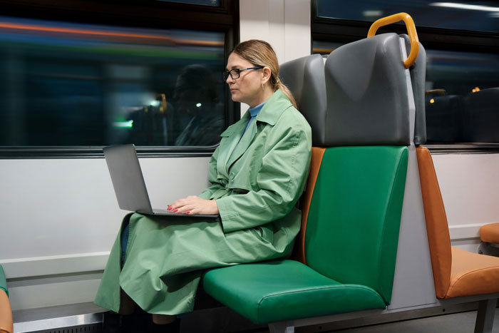 A woman in a green coat uses a laptop on a train seat, emphasizing the concept of prepaid train seat usage. A woman in a green coat uses a laptop on a train seat, emphasizing the concept of prepaid train seat usage.