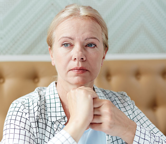 Woman looking thoughtful, sitting indoors, wearing a checkered shirt. Keywords: horrible mother. Woman looking thoughtful, sitting indoors, wearing a checkered shirt. Keywords: horrible mother.