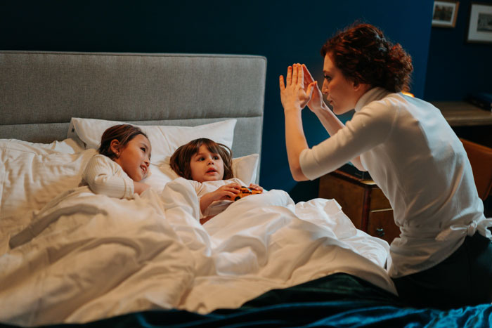 A woman entertains two children in bed, engaging in storytelling. A woman entertains two children in bed, engaging in storytelling.