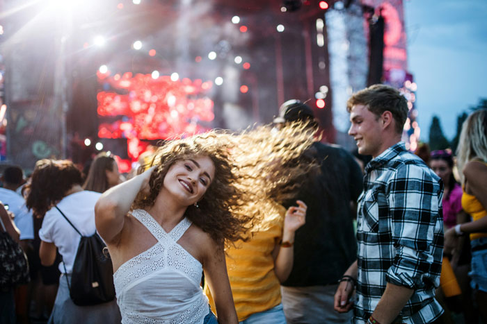 People enjoying a concert, with energetic dancing and vibrant stage lights in the background. People enjoying a concert, with energetic dancing and vibrant stage lights in the background.