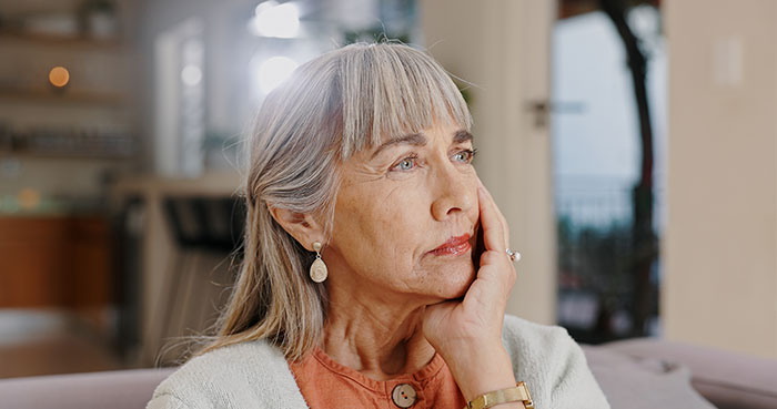 A contemplative older woman sitting on a sofa, wearing earrings and a watch, in a bright room. A contemplative older woman sitting on a sofa, wearing earrings and a watch, in a bright room.