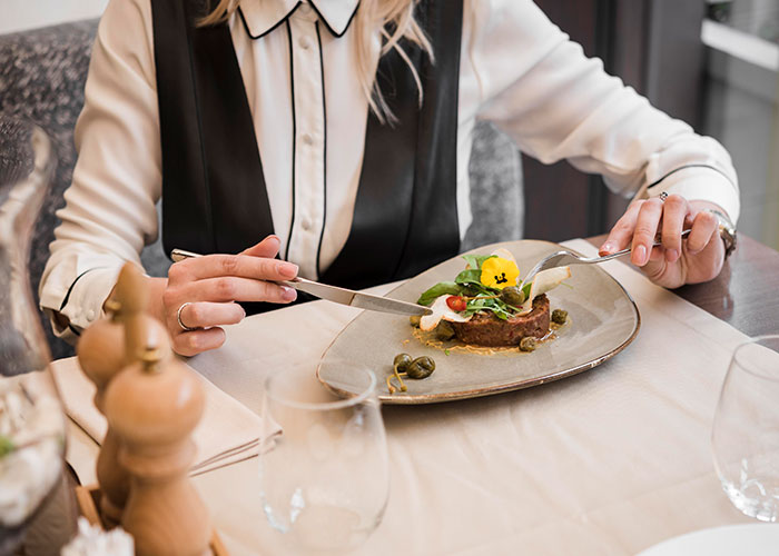 A person dining in a restaurant, illustrating ways restaurants manipulate spending with elegant meal presentation. A person dining in a restaurant, illustrating ways restaurants manipulate spending with elegant meal presentation.
