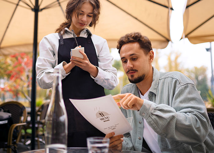 Man examining menu with waitress, illustrating restaurant manipulation tactics to encourage spending. Man examining menu with waitress, illustrating restaurant manipulation tactics to encourage spending.