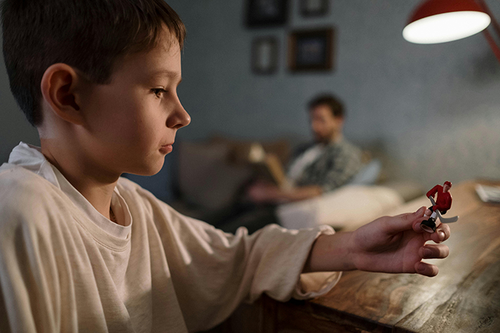 Child holding a toy while an adult reads in the background, related to a roommate and food allergy incident. Child holding a toy while an adult reads in the background, related to a roommate and food allergy incident.