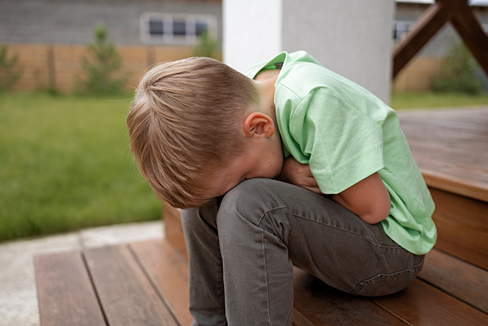 A young boy in a green shirt sitting on wooden steps, appearing upset or sad. A young boy in a green shirt sitting on wooden steps, appearing upset or sad.