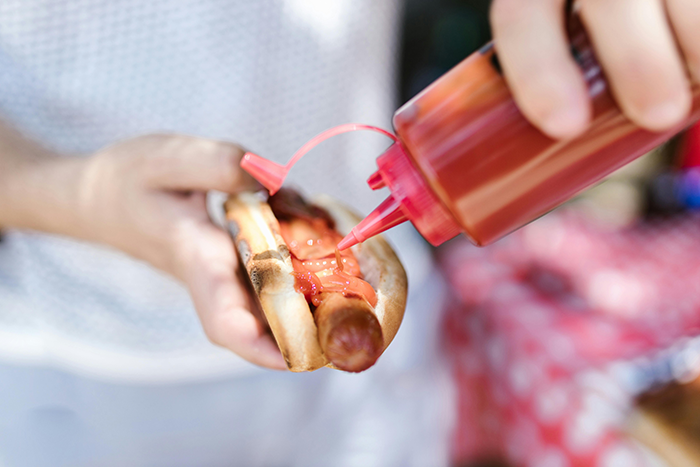 Person adding ketchup to a hotdog, with mozzarella hater theme. Person adding ketchup to a hotdog, with mozzarella hater theme.