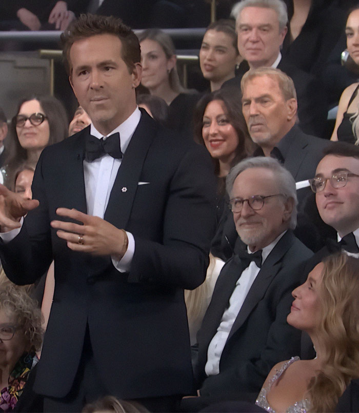 Ryan Reynolds in a tuxedo at SNL 50 event, with crowd reacting in the background. Ryan Reynolds in a tuxedo at SNL 50 event, with crowd reacting in the background.