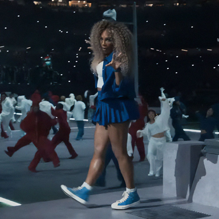 Person in a blue outfit performing at a stadium event. Person in a blue outfit performing at a stadium event.