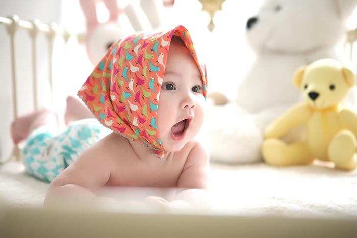 Baby with colorful scarf, lying in crib next to stuffed animals; related to babysitting and family dynamics. Baby with colorful scarf, lying in crib next to stuffed animals; related to babysitting and family dynamics.