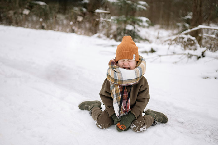 Child sitting in snow wearing a warm outfit and giggling, related to beginner ski trail mishap. Child sitting in snow wearing a warm outfit and giggling, related to beginner ski trail mishap.