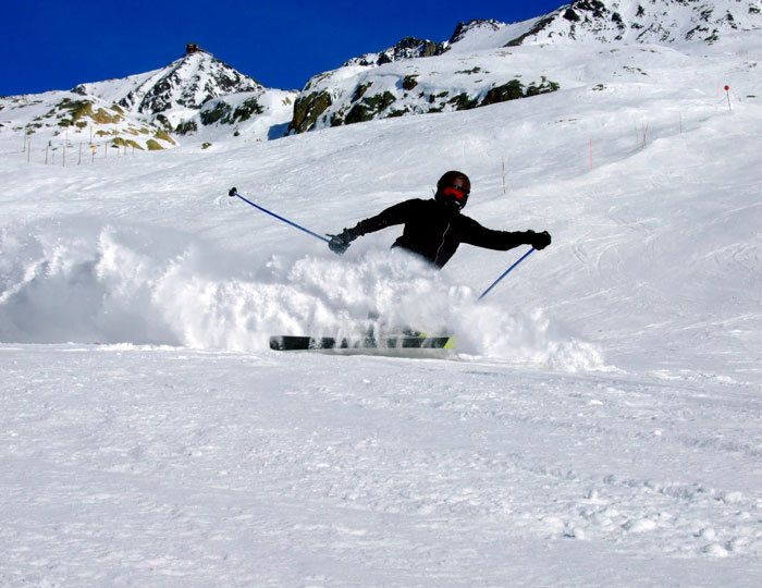 Skier on snowy trail with mountains in the background, wearing black gear, mid-turn, creating snow spray. Skier on snowy trail with mountains in the background, wearing black gear, mid-turn, creating snow spray.