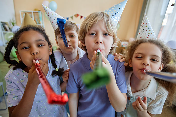 Children at a party wearing hats, blowing noisemakers, with siblings and no presents visible. Children at a party wearing hats, blowing noisemakers, with siblings and no presents visible.