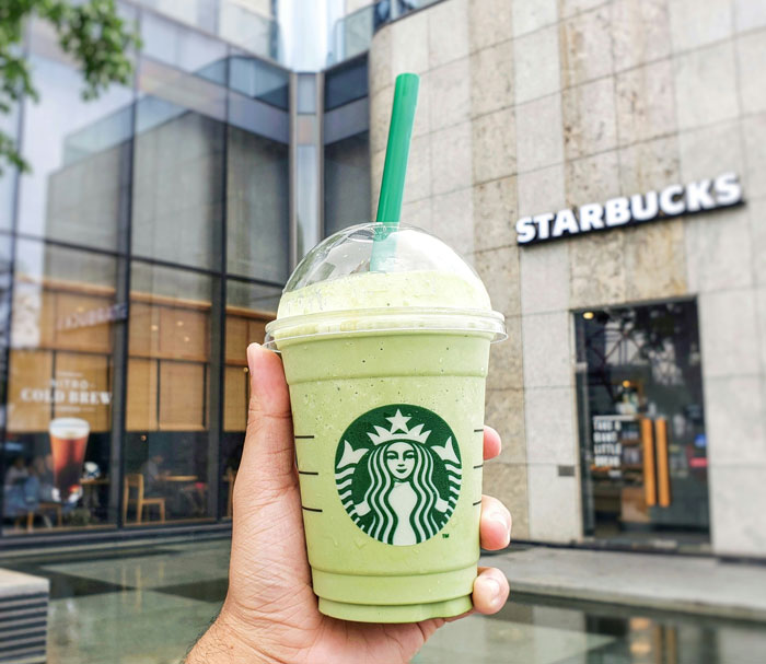Person holding a green Starbucks drink outside a store, featuring upcoming menu update. Person holding a green Starbucks drink outside a store, featuring upcoming menu update.
