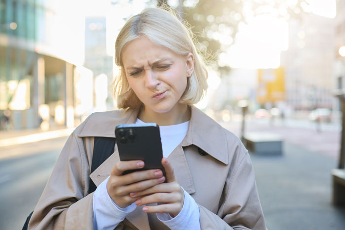 Woman reacting to a message on her phone outdoors, related to a birthday trip and babysitting discussion. Woman reacting to a message on her phone outdoors, related to a birthday trip and babysitting discussion.