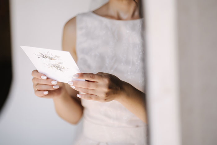 Bride holding a wedding invitation, reflecting on family dynamics surrounding her wedding day. Bride holding a wedding invitation, reflecting on family dynamics surrounding her wedding day.