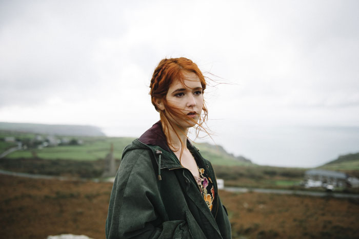 Woman with red hair standing outdoors, wearing a green jacket, with a scenic landscape in the background. Woman with red hair standing outdoors, wearing a green jacket, with a scenic landscape in the background.