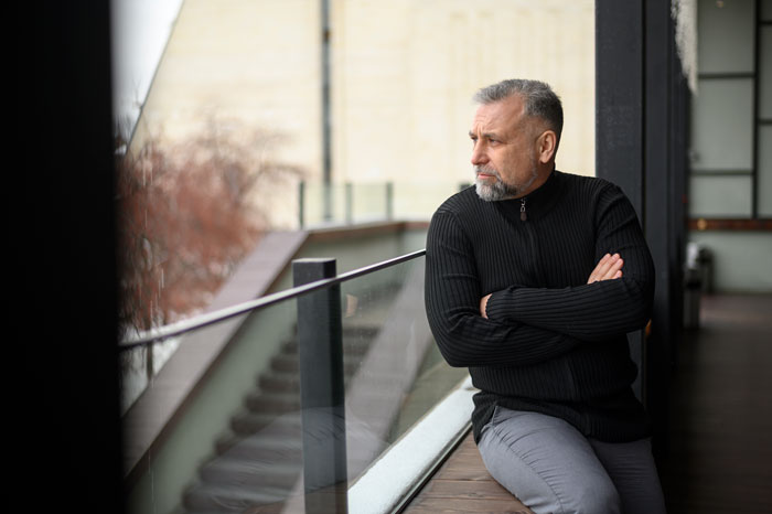 A man in a black sweater looking pensive while seated indoors, reflecting on choosing wife over daughter for wedding decision. A man in a black sweater looking pensive while seated indoors, reflecting on choosing wife over daughter for wedding decision.