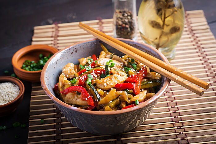 Multi-functional bowl of stir-fried chicken and vegetables with chopsticks, placed on a bamboo mat.