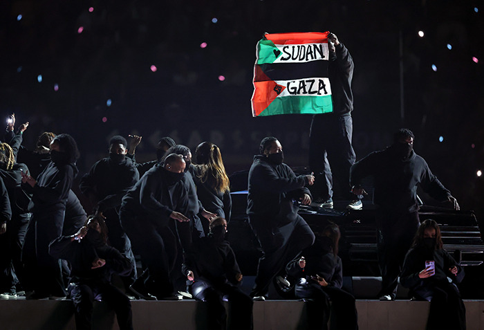 Super Bowl dancer displays flag with messages for Sudan and Gaza during halftime show, amid performance. Super Bowl dancer displays flag with messages for Sudan and Gaza during halftime show, amid performance.