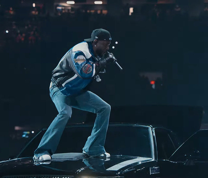 Kendrick Lamar. performing on a stage, wearing a cap and jacket, under dramatic lighting. Kendrick Lamar. performing on a stage, wearing a cap and jacket, under dramatic lighting.