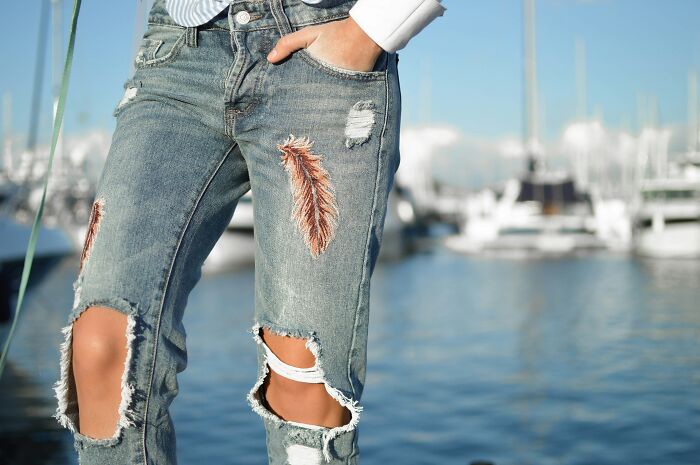 Ripped jeans with embroidery, a recent fashion trend people hate, worn by a person near a marina.