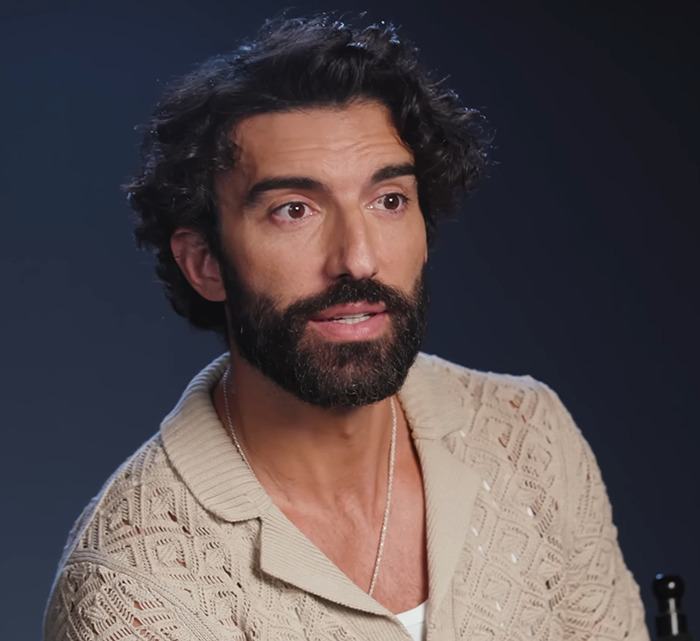 Justin Baldoni in a beige cardigan discusses a topic in front of a dark background. Justin Baldoni in a beige cardigan discusses a topic in front of a dark background.