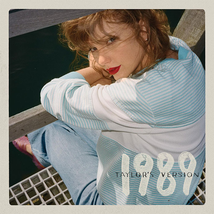 Taylor Swift sitting by water, wearing a striped sweater and jeans, featuring '1989 Taylor's Version' text. Taylor Swift sitting by water, wearing a striped sweater and jeans, featuring '1989 Taylor's Version' text.