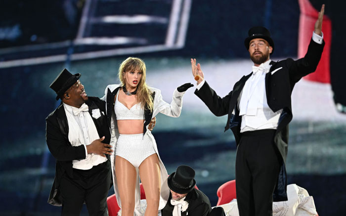 Taylor Swift and Travis Kelce perform on stage in elegant costumes, engaging audiences with a lively dance routine.