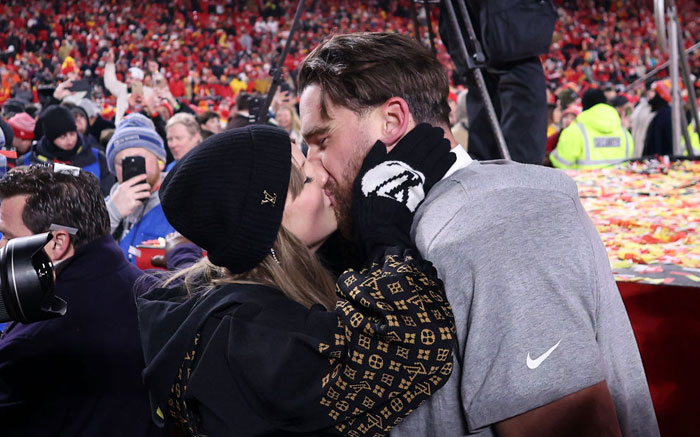 Taylor Swift and Travis Kelce sharing a kiss in a crowded stadium, surrounded by cheering fans and confetti.