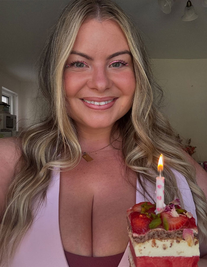 Woman smiling with a lit candle on a cake, addressing stares at her G-cup size confidently. Woman smiling with a lit candle on a cake, addressing stares at her G-cup size confidently.