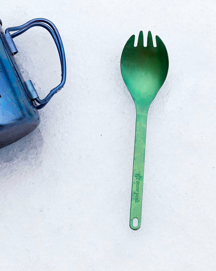 Green spork and blue mug on a white surface, showcasing multi-functional minimalist utensils.