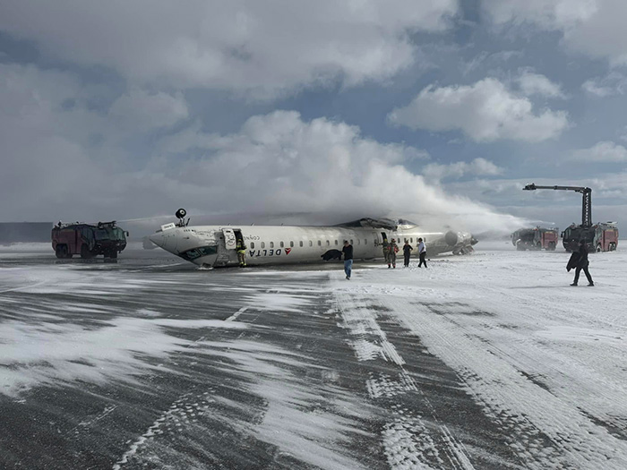 Emergency landing response with plane on snowy runway; firefighters and vehicles present. Emergency landing response with plane on snowy runway; firefighters and vehicles present.