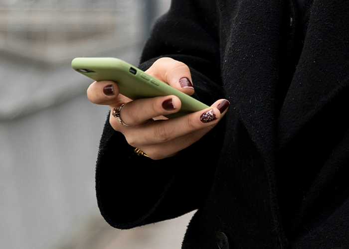 Woman in a black coat holding a smartphone, displaying a message about daughter wearing a suit to prom. Woman in a black coat holding a smartphone, displaying a message about daughter wearing a suit to prom.