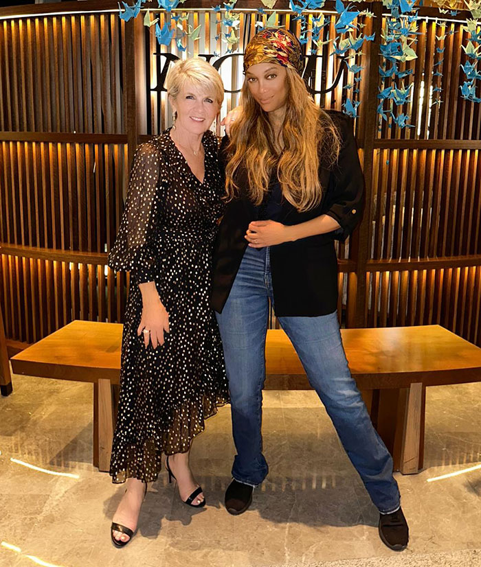 Two women smiling indoors with a wooden backdrop and hanging decorations. Two women smiling indoors with a wooden backdrop and hanging decorations.