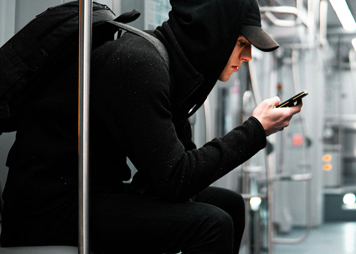 Person in a hoodie using a phone on public transport, emphasizing phone number privacy. Person in a hoodie using a phone on public transport, emphasizing phone number privacy.