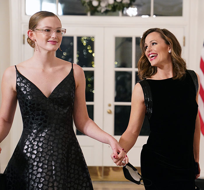 Two women, elegantly dressed, holding hands and smiling in a well-lit room. Two women, elegantly dressed, holding hands and smiling in a well-lit room.