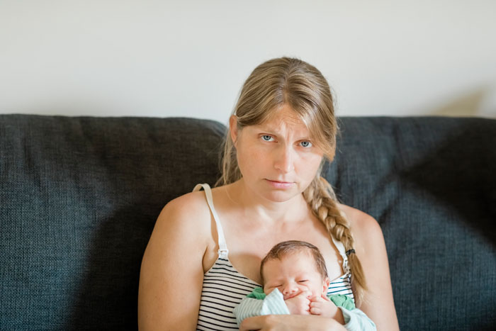 Woman sitting on a couch with a newborn baby, looking upset. Woman sitting on a couch with a newborn baby, looking upset.