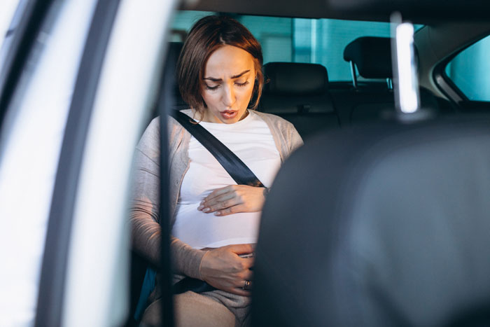 Pregnant woman in labor, sitting in a car, holding her belly with a concerned expression. Pregnant woman in labor, sitting in a car, holding her belly with a concerned expression.