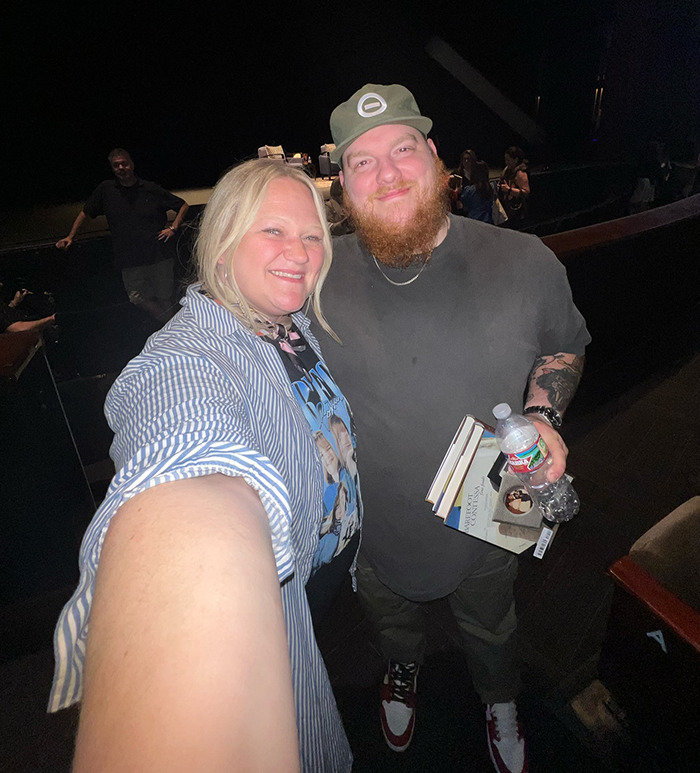 Husband and wife posing for a selfie in a theater, man holding books and a water bottle, related to viral shower clip story. Husband and wife posing for a selfie in a theater, man holding books and a water bottle, related to viral shower clip story.