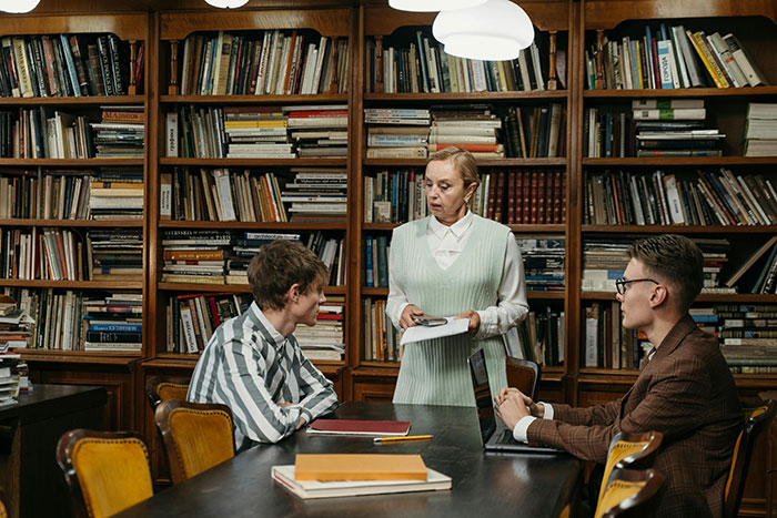 A woman in an office library addressing two coworkers, highlighting a workplace interaction. A woman in an office library addressing two coworkers, highlighting a workplace interaction.