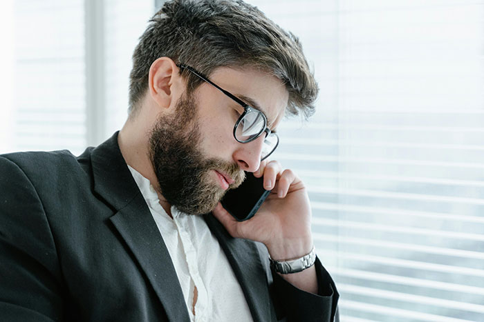 A man in a suit and glasses on the phone, by a window in an office setting, appearing thoughtful. A man in a suit and glasses on the phone, by a window in an office setting, appearing thoughtful.