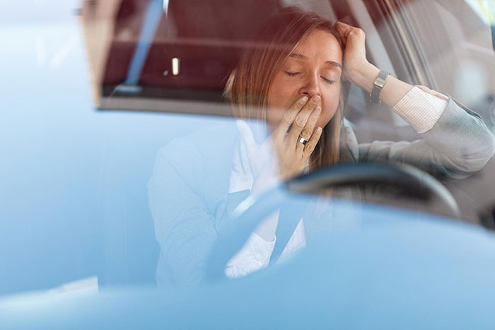 Tired woman sitting in a car, covering her mouth with one hand, appearing stressed. Tired woman sitting in a car, covering her mouth with one hand, appearing stressed.